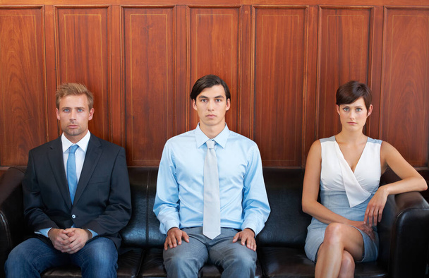 Momentos de ansiedad antes de la entrevista. Retrato de tres jóvenes vestidos formalmente y sentados en un sofá - Foto, imagen