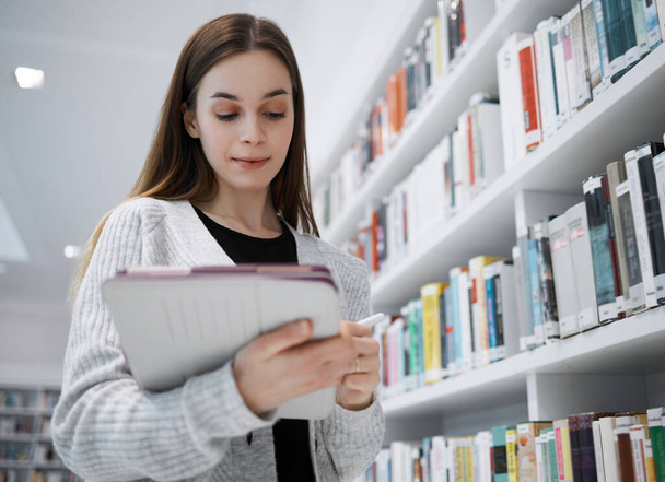 University, writing or woman in library with tablet for research, education or learning. Bookshelf, books or girl student on tech for scholarship search or planning school project at collage campus. - Fotografie, Obrázek