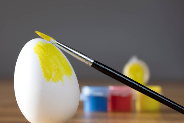 rough brush is painting a fragile easter egg with Yellow color, prepering for Holiday Happy Easter concept closeup colorful hobby - Photo, Image