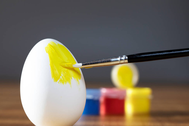 rough brush is painting a fragile easter egg with Yellow color, prepering for Holiday Happy Easter concept closeup colorful hobby - Фото, изображение