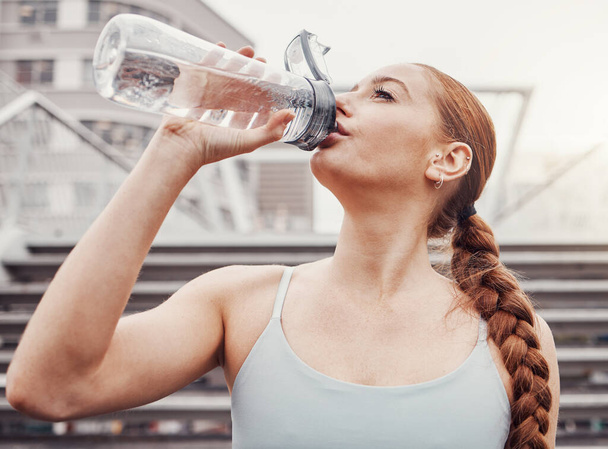 Фитнес, гидратация и спортивная женщина пьют воду на открытом воздухе в городе во время кардио или упражнений на выносливость. Бегунья, тренировка и увлажнение с женщиной-спортсменкой, тренирующейся в городском городе для здоровья. - Фото, изображение