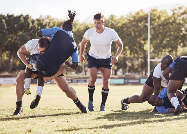 Kaukasischer Rugbyspieler, der während eines Rugbyspiels draußen auf dem Spielfeld versucht, einen Gegner anzugreifen. Junger athletischer Mann, der einen Gegner angreift, um ihn am Toreschießen zu hindern. Letzte Verteidigungslinie. - Foto, Bild