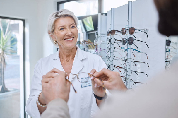 Glasses, retail store and sale of a senior eye doctor holding a frame to help customer shopping. Happy optometrist, shop wellness and service of an elderly eyes expert with eyeglasses vision check. - Fotoğraf, Görsel