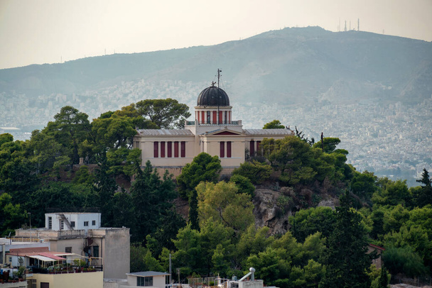 L'Osservatorio Nazionale della città di Atene, in Grecia, in cima alla collina delle Ninfe nel distretto di Thission. Vista dal distretto di Plaka sotto l'Acropoli di Atene. Giorno soleggiato, Atene sullo sfondo - Foto, immagini