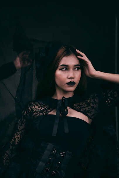 アジアの10代の若者は、夜にハロウィーンの前に魔女のような黒い化粧と黒いドレスで恐ろしい外観をしています - 写真・画像