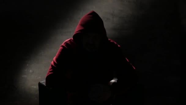 Anonimowy mężczyzna na nagraniu z przesłuchania w kapturze, tajemniczy mężczyzna siedzący na krześle i mówiący. Anonimowy wywiad bez widocznych zdjęć twarzy - Materiał filmowy, wideo