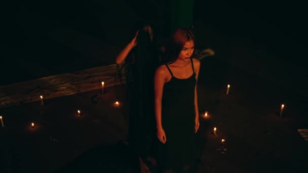 una mujer con un vestido negro se pone una túnica negra mientras realiza un ritual de adoración al diablo en la oscuridad por la noche - Imágenes, Vídeo