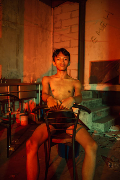 a teenager in short black pants was sitting in an unused warehouse with lots of chairs at night - 写真・画像