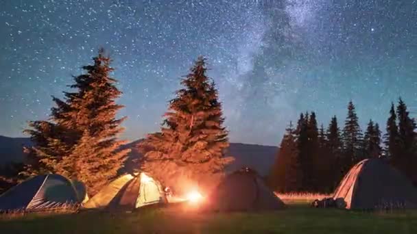 Night camping with five tourists illuminated tents. Hiker having a rest near campfire and forest, cooking dinner on fire. Timelapse of the starry sky with the Milky Way. Concept of tourism and nature. - Footage, Video