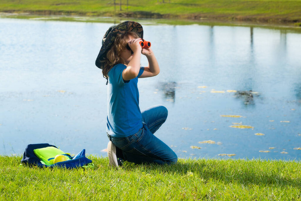 Little child with backpack and binoculars. Imagination or exploration in park. Happy child playing with binocular. Young tourist explorer. Child vacation and travel. Summer journey for kids - Photo, Image
