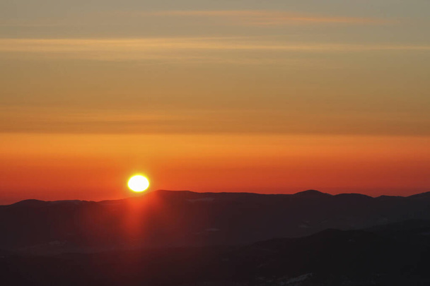 Orange sky and sun disc at sunrise in dark winter mountains, Carpathians - Photo, image