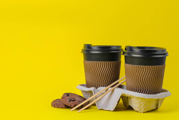 Tasses en papier avec café sur un stand et biscuits aux pépites de chocolat sur fond jaune. café à emporter - Photo, image