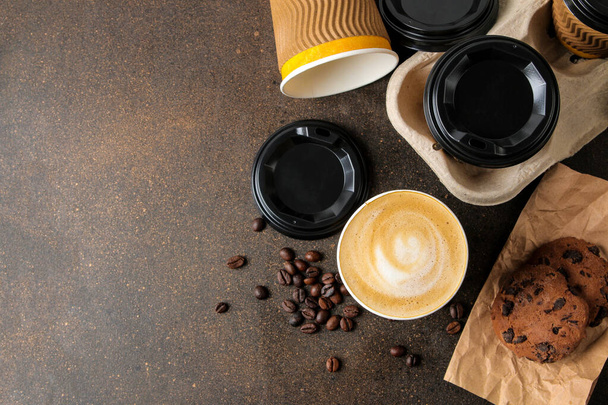 Papírpoharak cappuccinóval a lelátón, kávébab és csokis süti a barna asztalon. Kávét elvitelre. - Fotó, kép