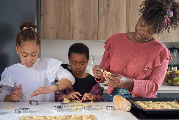 Αφρικανική οικογένεια κοπής μπισκότων σχήματα σε μια ζύμη μπισκότων στην κουζίνα. Οριζόντια διευρυμένη οικογένεια. - Φωτογραφία, εικόνα