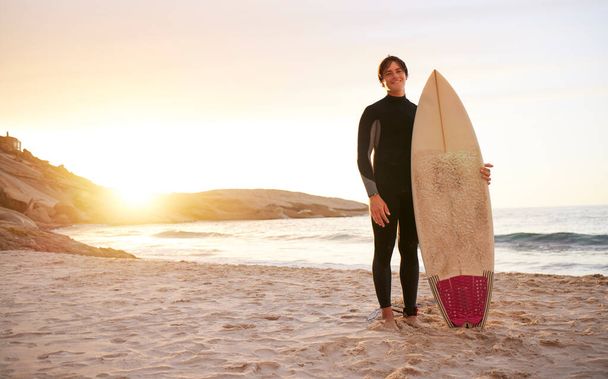Surfer, portrait and man with surfboard at the sea, beach and ocean in sunset or the morning with mockup space. Young, ready and male in swimsuit on a sunny surf day on the sand, shore and water. - Photo, image