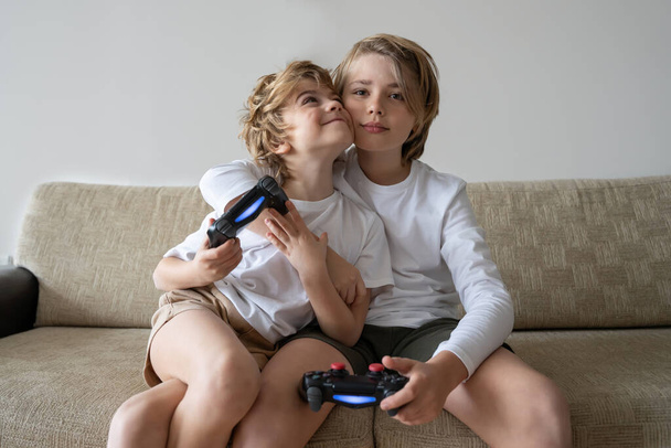 Cute children joyful playing video games with controller console, brother sister expressing emotions while enjoying their hobby playstation joystick - 写真・画像