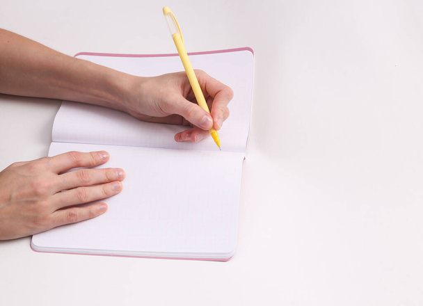 Το θηλυκό αριστερό χέρι γράφει σε ένα άδειο σημειωματάριο σε γκρι φόντο. Αριστερό. - Φωτογραφία, εικόνα