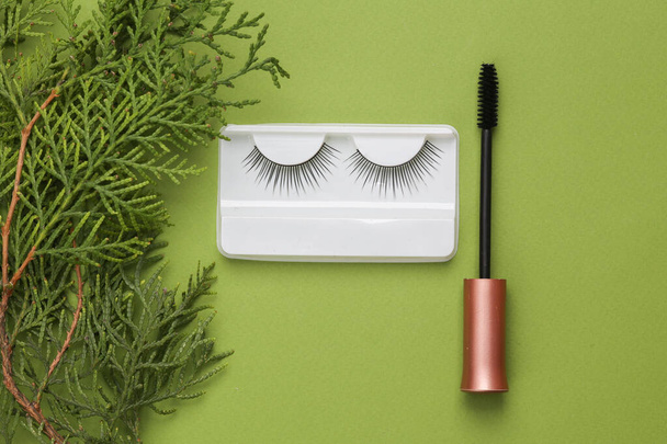 Aesthetic still life false eyelashes with mascara brush and fir twig on green background. Top view - Photo, Image