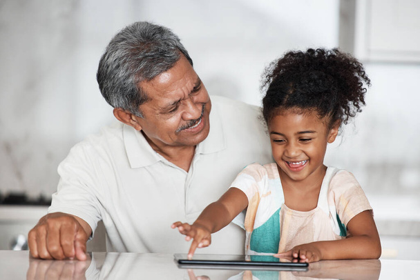 Uczenie się, dziadek i dziewczyna z tabletem w domu, grając w gry online lub aplikacji edukacyjnej. Tworzenie więzi rodzinnych, ekran dotykowy lub opieka nad szczęśliwym dziadkiem uczącym dziecko, jak korzystać z technologii cyfrowej w domu. - Zdjęcie, obraz