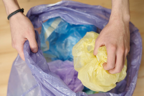 Genç bir adam ya da gencin elleri çeşitli çöpleri ayırırken buruşmuş plastik torbaları atık poşetlere dolduruyor. - Fotoğraf, Görsel
