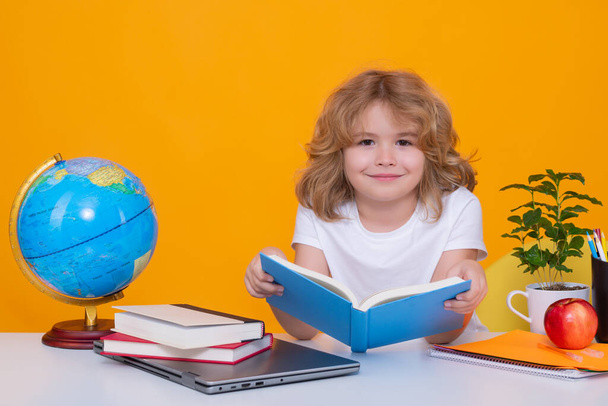 Шкільна дитина читає книжку. Повернутися до школи. Смішний хлопчик з початкової школи з книгою. Портрет школяра ізольовано на жовтому фоні студії. Освіта
 - Фото, зображення