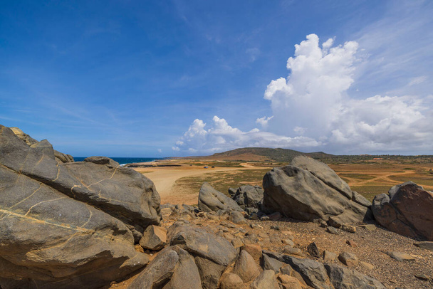 Großaufnahme von großen Felsen in der Wüste an der Karibikküste vor blauem Himmel mit weißen Wolken Insel Aruba. - Foto, Bild