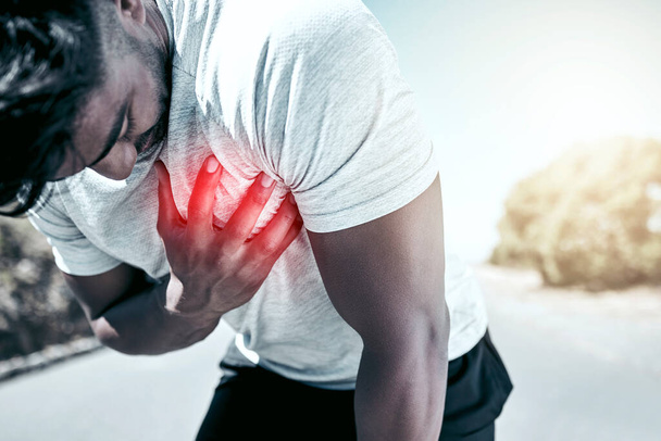 Closeup fit mixed race man holding his chest in pain while exercising outdoors. Unrecognizable male athlete struggling to breath, having a heart attack or going into cardiac arrest, highlighted by cg. - Fotó, kép