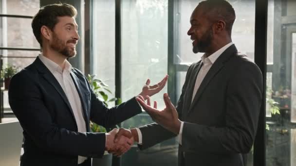 Caucasian boss hr manager man shake hand of African American candidate partner client making deal hiring thanking for collaboration congratulation. Diverse business partners men in office handshaking - 映像、動画