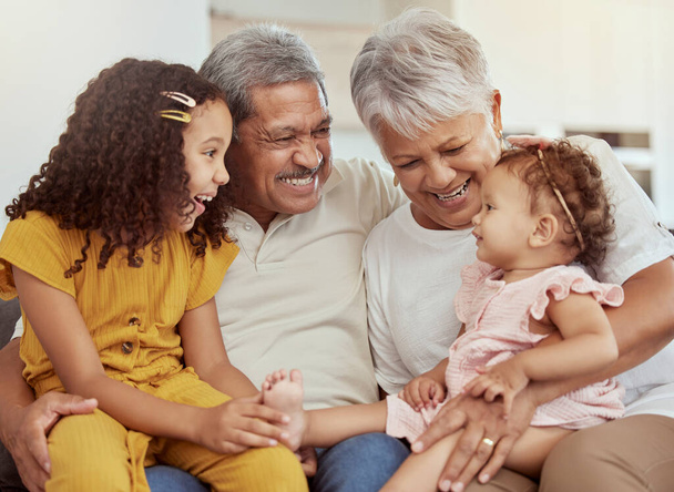 Mixed race grandparents enjoying weekend with granddaughters in home living room. Adorable smiling hispanic girls bonding with grandmother and grandfather. Happy seniors and children sitting together. - Foto, imagen