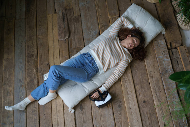 Sanal gerçeklik gözlüklü kadın evde ahşap zeminde uyuyor. Sakin genç bayan rahat bir yatakta uzanıp uzun bir günün ardından sağlık ve sağlık için kestiriyor. - Fotoğraf, Görsel
