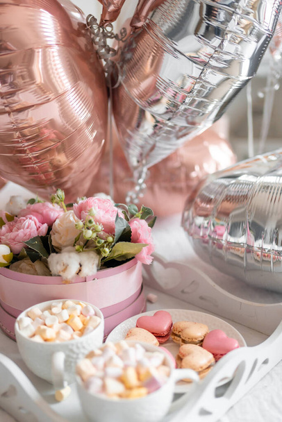 Blumen und Süßigkeiten auf weißem Tisch und Luftballons auf weißem Bett. Geschenk zum Valentinstag oder 8. März oder Muttertag oder Geburtstag. Hochwertiges Foto - Foto, Bild