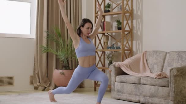 Entrenador de yoga en traje azul haciendo ejercicios para calentar el cuerpo. Mujer joven practica yoga y estiramiento en una oficina minimalista. Concepto de yoga y estiramiento. - Metraje, vídeo