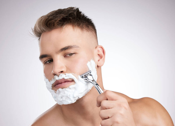Ця бритва чудово справляється. Студійний знімок молодого чоловіка, що голиться обличчям на сірому фоні
 - Фото, зображення