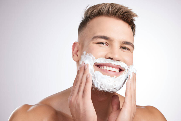 Бороди мусять йти. Студійний знімок молодого чоловіка, який наносить крем для гоління на обличчя на сірий фон
 - Фото, зображення