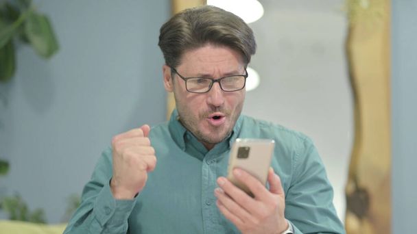Excited Middle Aged Businessman Celebrating Win on Smartphone - Foto, immagini