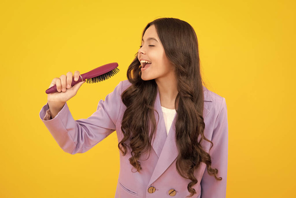 Excited fun teenager girl singing with comb. Child girl with brush combing hair. Girl taking haircare and hairstyle - Foto, imagen