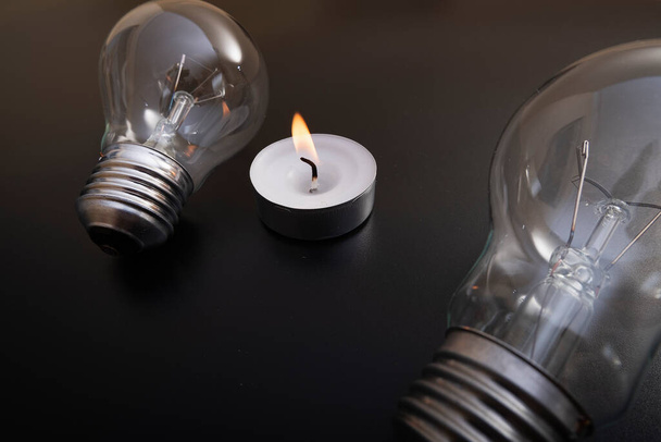 Electric lamp and candle on a dark background.  Incandescent bulb and candle. Power cut or power outage. High electricity prices. Saving electricity. Symbol of return to the past. - Photo, Image
