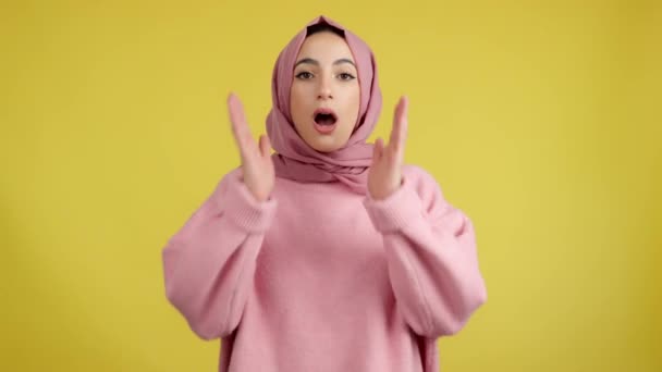 Překvapený muslim žena v hidžábu při pohledu na kameru ve studiu se žlutým pozadím - Záběry, video