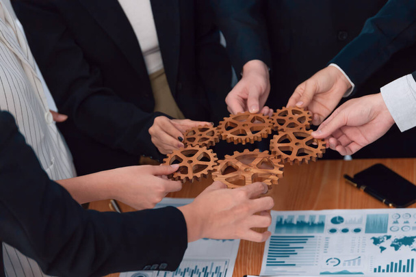 Closeup top view businesspeople hand holding gear and join together over meeting table with financial report papers. Cohesive group of office workers holding cog wheel as synergy harmony concept. - Valokuva, kuva