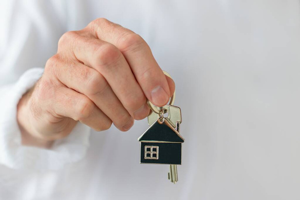 Το χέρι ενός άντρα κρατάει το κλειδί του σπιτιού. Έννοια της αγοράς ενός νέου σπιτιού ή σπιτιού. - Φωτογραφία, εικόνα