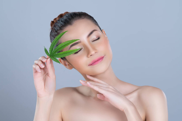 Closeup glamorous beautiful woman with soft make up and flawless smooth clean skin holding green leaf. Cannabis skincare cosmetic product for natural skin treatment concept in isolated background - Fotó, kép