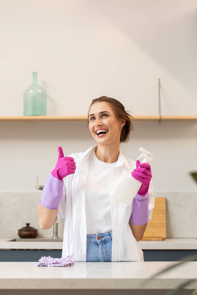 Attractive housewife holds a spray bottle with cleaning agent in her hand and shows a thumbs up. The concept of home cleaning, cleaning service. - Foto, afbeelding