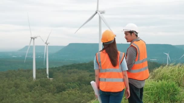 Mannelijke en vrouwelijke ingenieurs werken op een windmolenpark op de top van een heuvel of berg op het platteland. Progressief ideaal voor de toekomstige productie van hernieuwbare, duurzame energie. - Video