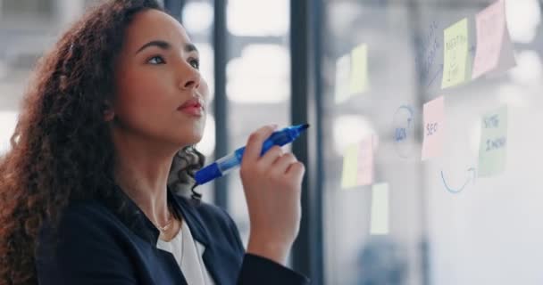 Business woman, thinking and planning schedule for strategy, brainstorming or tasks at office. Female employee designer contemplating project idea, writing or sticky note on glass window at workplace. - Filmati, video