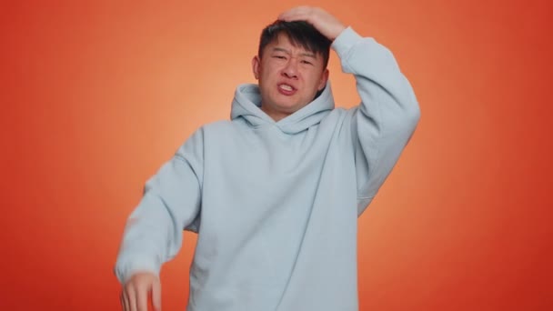 Handsome asian man feeling hopelessness loneliness, nervous breakdown, loses becoming surprised by lottery results, bad fortune, loss, unlucky news. Chinese guy isolated on studio orange background - Materiał filmowy, wideo