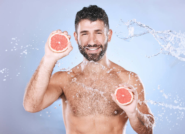 Grapefruit, water splash and man on blue background for wellness benefits, beauty and skincare. Male model, portrait and citrus fruits for vitamin c cosmetics, detox and nutrition for healthy shower. - Zdjęcie, obraz