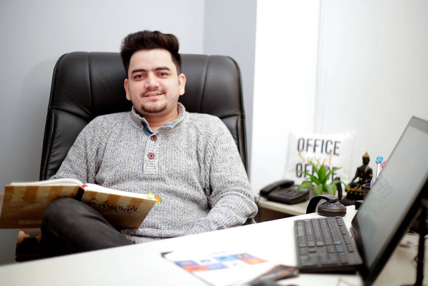 A young businessman is sitting on chair at office and smiling. - Foto, Imagen