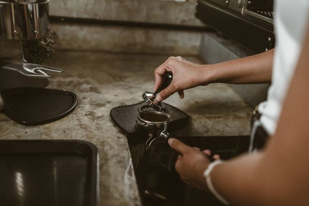 Barista using a tamper to press ground coffee into a portafilter. Coffee maker concept - Фото, зображення