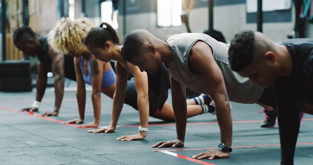 Staying focused in order to grow stronger. a group of sporty young people doing pushups together in a gym - Foto, imagen