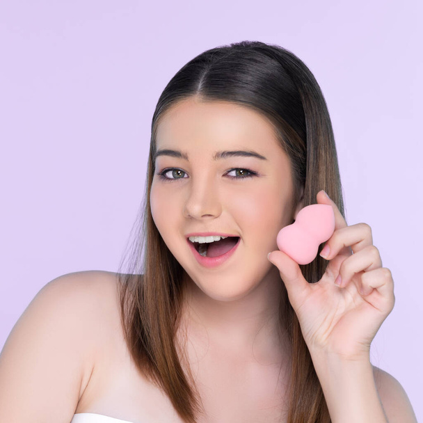 Facial cosmetic makeup concept. Portrait of young charming girl applying dry powder foundation. Beautiful girl smiling with perfect skin putting cosmetic makeup on her face. - Photo, Image